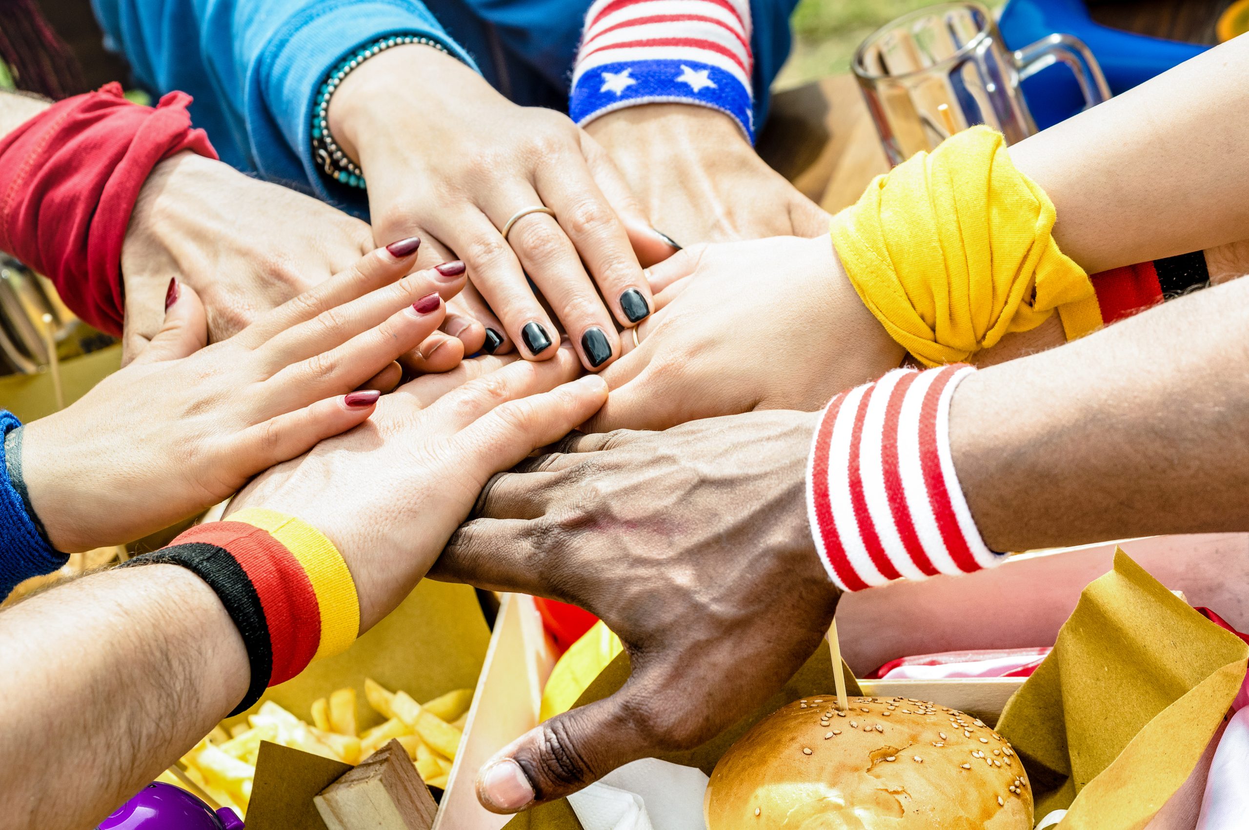 Top side view of multiracial hands of football supporter friend sharing street food - Friendship concept with soccer fan enjoying food together - People eating at party bar pub after sport match event